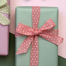 Load image into Gallery viewer, A wrapped rectangular gift box in pale mint green with a wide dusty pink polka-dot ribbon tied in a bow, set against a soft pink and dark green background.