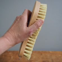 Load image into Gallery viewer, Hand holding a wooden brush with bristles against a gray background