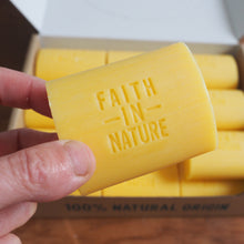Load image into Gallery viewer, Yellow bar of soap with 'Faith in Nature' branding held by a hand, against a wooden background.