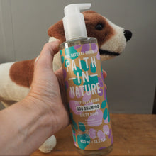 Load image into Gallery viewer, A hand holds a bottle of Faith In Nature Deep Cleansing Dog Shampoo in front of a brown and white plush dog toy, with a neutral indoor background.