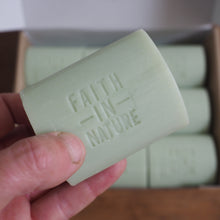 Load image into Gallery viewer, Hand holding a green bar of soap with 'Faith in Nature' branding, in front of a box containing more bars.