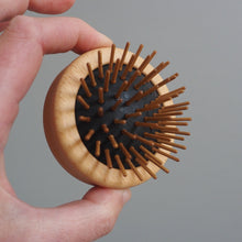 Load image into Gallery viewer, Hand holding a wooden hairbrush against a gray background