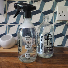 Load image into Gallery viewer, Two clear glass cleaning spray bottles with black labels and a trigger sprayer, displayed on a wooden surface against a blue and white geometric tiled wall.