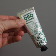 Load image into Gallery viewer, Hand holding a tube of 'DEO' balm with green text on a gray background
