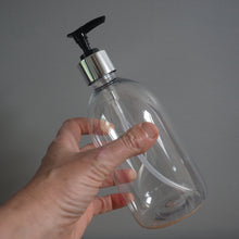 Load image into Gallery viewer, Clear soap dispenser with black pump held by a hand against a gray background