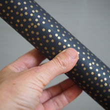 Load image into Gallery viewer, A close-up of a hand holding a black cylindrical rod or tube covered in evenly spaced small gold polka dots, against a plain light gray background.