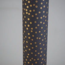 Load image into Gallery viewer, A close-up of a cylindrical product, likely a vase or candle holder, covered in a dark charcoal gray or black material with a repeating pattern of small metallic gold polka dots, set against a plain light gray background.