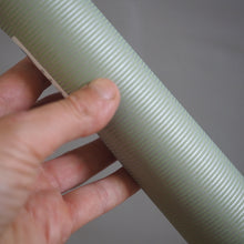 Load image into Gallery viewer, A close-up of a hand holding a ribbed, corrugated light sage green plastic tube against a neutral gray background.