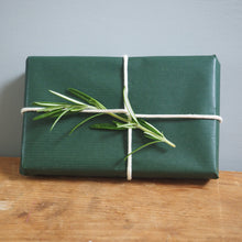 Load image into Gallery viewer, Green wrapped gift with a sprig of rosemary on a wooden surface and gray background