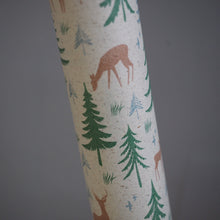 Load image into Gallery viewer, A close-up of a cylindrical product, likely a roll of wrapping paper or a decorative tube, featuring a rustic forest pattern with green pine trees, brown deer, and small blue birds on a textured off-white background, set against a solid dark gray backdrop.