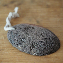 Load image into Gallery viewer, A dark gray pumice stone ornament with a white hanging string, resting on a wooden surface.