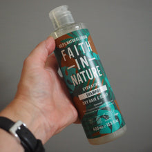 Load image into Gallery viewer, Hand holding a bottle of Faith in Nature shampoo against a gray background