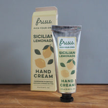 Load image into Gallery viewer, A tube and box of fru. Sicilian Lemonade Hand Cream standing on a wooden surface against a gray wall.