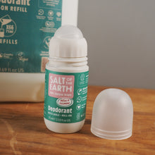 Load image into Gallery viewer, A Salt of the Earth roll-on deodorant refill bottle with its cap removed, sitting on a wooden tabletop with the product box blurred in the background.