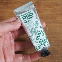 Load image into Gallery viewer, A hand holding a squeeze tube of Bergamot Deo Hand Balm against a wooden tabletop background.