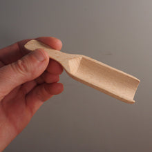 Load image into Gallery viewer, A hand holding a small, unfinished light-colored wooden scoop or miniature shovel against a plain gray background.
