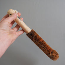 Load image into Gallery viewer, Hand holding a bottle brush with a wooden handle and brown bristles against a gray background