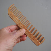 Load image into Gallery viewer, Hand holding a wooden comb against a gray background
