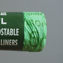 Load image into Gallery viewer, Hand holding a roll of compostable caddy liners with a gray background
