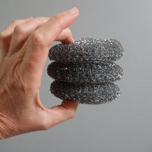 Load image into Gallery viewer, Hand holding a stack of metal sponges against a gray background
