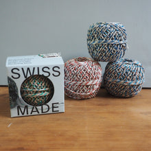 Load image into Gallery viewer, Three balls of multicolored yarn and a box labeled 'Swiss Made' on a wooden surface.
