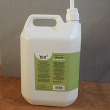 Load image into Gallery viewer, A large white plastic dispenser bottle with a pump, shown lying on a wooden surface next to a gray sheet. The bottle has a green label with the brand name Bio.
