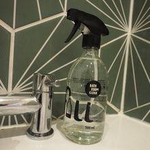 Load image into Gallery viewer, A clear plastic spray bottle of hand wash with a black trigger sprayer, labeled 'all in one hand wash' and '300ml', resting against a chrome faucet on a green and white geometric tiled surface.

