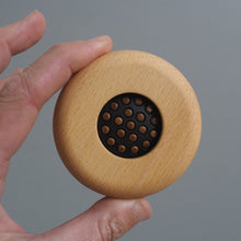 Load image into Gallery viewer, Hand holding a wooden object with a central black circular component against a gray background
