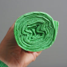 Load image into Gallery viewer, Hand holding a roll of green paper against a gray background
