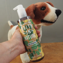 Load image into Gallery viewer, A hand holds a bottle of Faith In Nature Gentle Dog Shampoo in front of a plush beagle toy on a wooden table.
