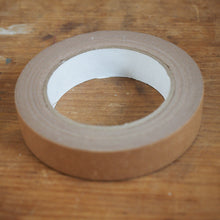 Load image into Gallery viewer, A roll of brown tape with a white inner core, resting on a wooden tabletop.
