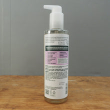 Load image into Gallery viewer, A clear plastic pump bottle of hair product with a white pump dispenser, standing upright on a wooden surface against a gray background.
