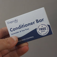 Load image into Gallery viewer, A hand holding a white and navy blue box of Friendly Soaps Conditioner Bar (Lavender &amp; Tea Tree) against a plain gray wall.
