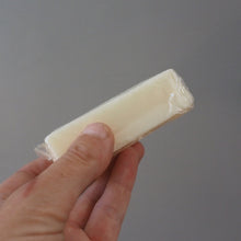 Load image into Gallery viewer, A hand holding a small, rectangular, off-white wrapped item against a plain gray background.
