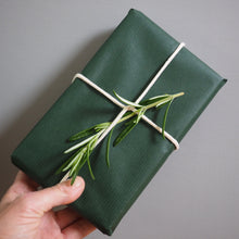 Load image into Gallery viewer, Hand holding a green wrapped gift with a sprig of rosemary against a gray background
