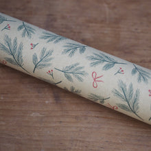 Load image into Gallery viewer, A close-up of a cylindrical drinking straw wrapped in beige holiday wrapping paper with a green pine branch and red bow pattern, resting on a wooden surface.
