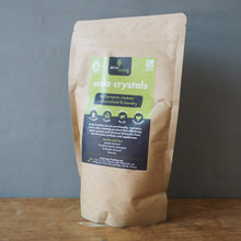 Load image into Gallery viewer, A stand-up kraft paper pouch of Solis Crystals bath salts, featuring a green and black label, standing on a wooden surface against a gray wall.
