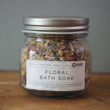 Load image into Gallery viewer, A glass jar of Organic Garden Brand 'Floral Bath Soak' with a silver metal lid, sitting on a wooden surface against a neutral gray background.
