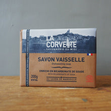 Load image into Gallery viewer, A 200g bar of La Corvete Savonne rie du Midi Savon Vaissele dishwashing soap, packaged in a brown cardboard box with a white and blue top label, standing on a wooden surface against a gray wall.
