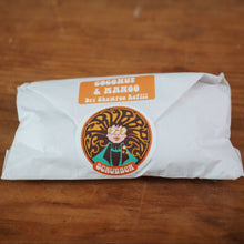 Load image into Gallery viewer, A white paper-wrapped shampoo bar with an orange label reading 'Coconut &amp; Mango Bri Shampoo Bar' and a circular Schumacher logo, placed on a wooden surface.
