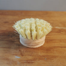 Load image into Gallery viewer, A small round brush with pale yellow bristles and a light beige wrapped base, placed on a wooden tabletop against a plain gray background.

