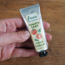 Load image into Gallery viewer, A hand holding a squeeze tube of fru. Pick Your Own Tomato Leaf Hand Cream against a wooden tabletop background.
