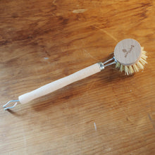 Load image into Gallery viewer, A small cleaning brush with a light wood handle, a round wooden head, and cream-colored bristles, resting on a wooden tabletop. The brand name 'Briarwood' is visible on the wooden head.
