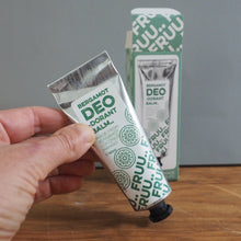 Load image into Gallery viewer, A hand holds a squeeze tube of Berganot Deo Dorant hand balm in front of its matching box on a wooden table against a gray wall.
