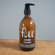 Load image into Gallery viewer, An amber glass pump bottle of fuli Hand Cream, featuring a black pump dispenser and white printed branding, set on a wooden surface against a plain gray background.
