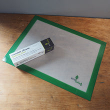 Load image into Gallery viewer, A green-bordered silicone baking mat with a white textured center, shown with its branded retail box on a wooden tabletop.
