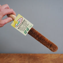 Load image into Gallery viewer, Bottle brush with LoofCo label held by a hand against a wooden surface and gray background
